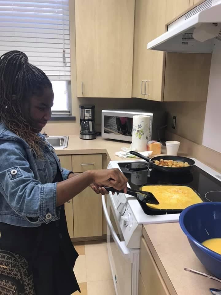 Middle-school aged girl cooking scrambled eggs in a frying pan on the stovetop.